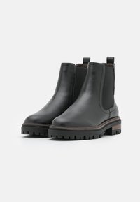 Botas Chelsea negras de cuero con paneles laterales elásticos, suela de tracción resistente y un acento de madera en el tacón. Textura de superficie suave.