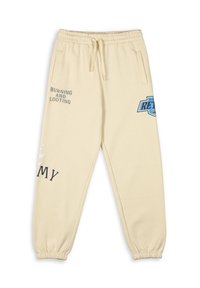 Beige Jogginghose mit einem Kordelzug, seitlichen Taschen und dem aufgedruckten Text "BURNING AND LOOTING" sowie einem blauen Logo auf dem Oberschenkel.