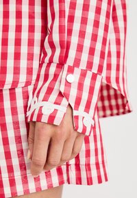 Rot-weißer Karoschirt mit Knopfmanschetten. Baumwollstoff mit kariertem Muster. Die Manschetten haben weiße gestickte Details.