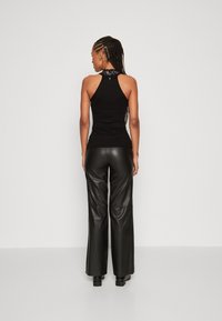 Crni halter top s uzorkovanim dekolteom, uparen s crnim kožnim hlačama visokog struka. Glatka tekstura i uski kroj.