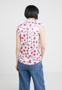 Vit blus med röda läpptryck och svart text, korta volangärmar och knäppning bak. Matchad med blå vida jeans.