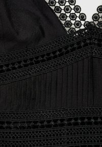 Tissu noir avec des détails en dentelle intricats, présentant des plis verticaux et des accents d'broderie texturée dans divers motifs.