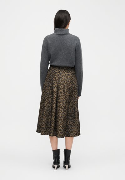 Γυναίκα που στέκεται με την πλάτη, φοράει γκρι πουλόβερ με ψηλό γιακά, καφέ midi φούστα με λεοπάρ σχέδιο και μαύρα μποτάκια με τακούνια.