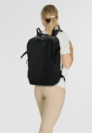 Schwarzer Rucksack mit glatter Textur, ausgestattet mit einem oberen Reißverschluss und verstellbaren Riemen. Branding in Grün auf der oberen linken Seite.