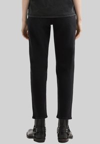 Pantalones de mezclilla negros con un corte recto, que presentan una cintura de altura media y un dobladillo que termina por encima del tobillo. Combinados con botas negras de tobillo.