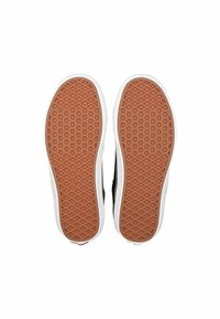 Zapatilla negra con suela de goma que presenta una textura con patrón de diamante y un ribete blanco alrededor de los bordes. El talón tiene un acento rojo.