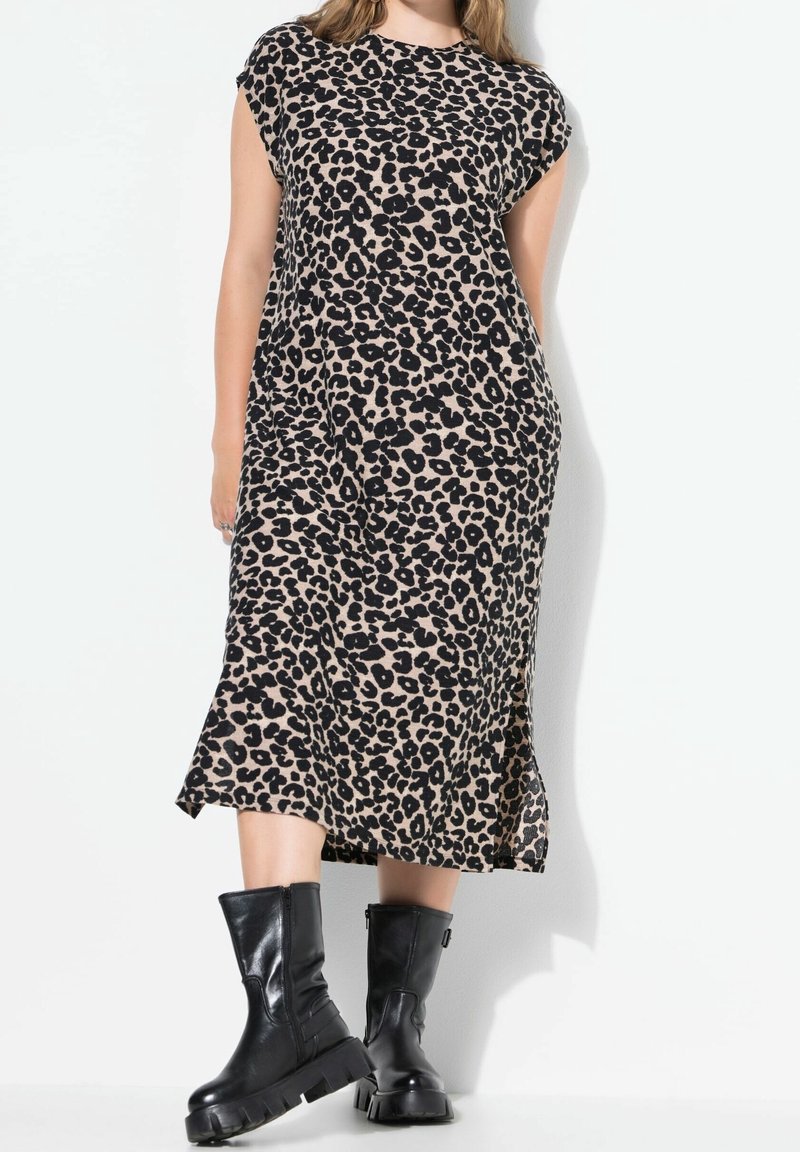 Femme portant une robe midi sans manches à imprimé léopard associée à des bottes montantes en cuir noir épaisses jusqu'à mi-mollet.