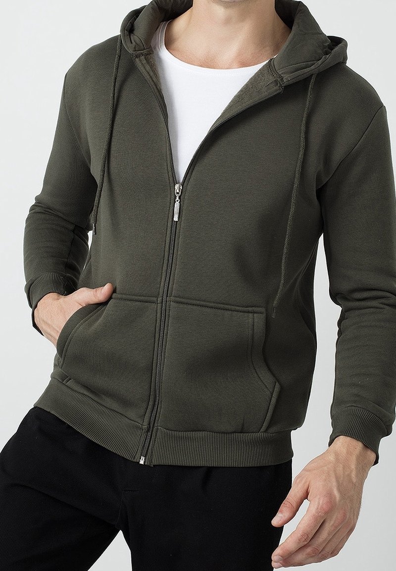 Sudadera con cremallera en color verde oliva, fabricada en suave algodón, que cuenta con una cremallera frontal, dos bolsillos laterales y puños y dobladillo acanalados.