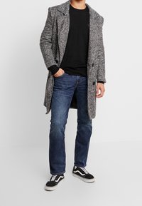 Gray textured overcoat with large black buttons, worn over a black sweater and blue jeans, paired with black and white sneakers.
