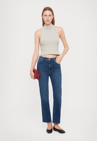 Top a costine senza maniche a righe sottili; jeans dritti blu scuro; ballerine nere; tiene in mano una piccola pochette rossa. Design semplice e moderno.