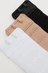 Tres tiras de tela elástica en negro, nude y blanco, cada una con cierres de gancho y ojo. Superficies texturizadas y bordes cosidos visibles.