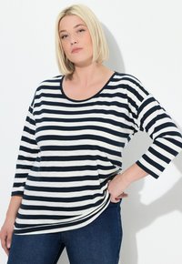 Marineblau und weiße gestreifte Langarmbluse mit rundem Ausschnitt und lockerer Passform, kombiniert mit dunkelblauen Jeans. Aus weichem Baumwollmaterial, ohne Verzierungen.