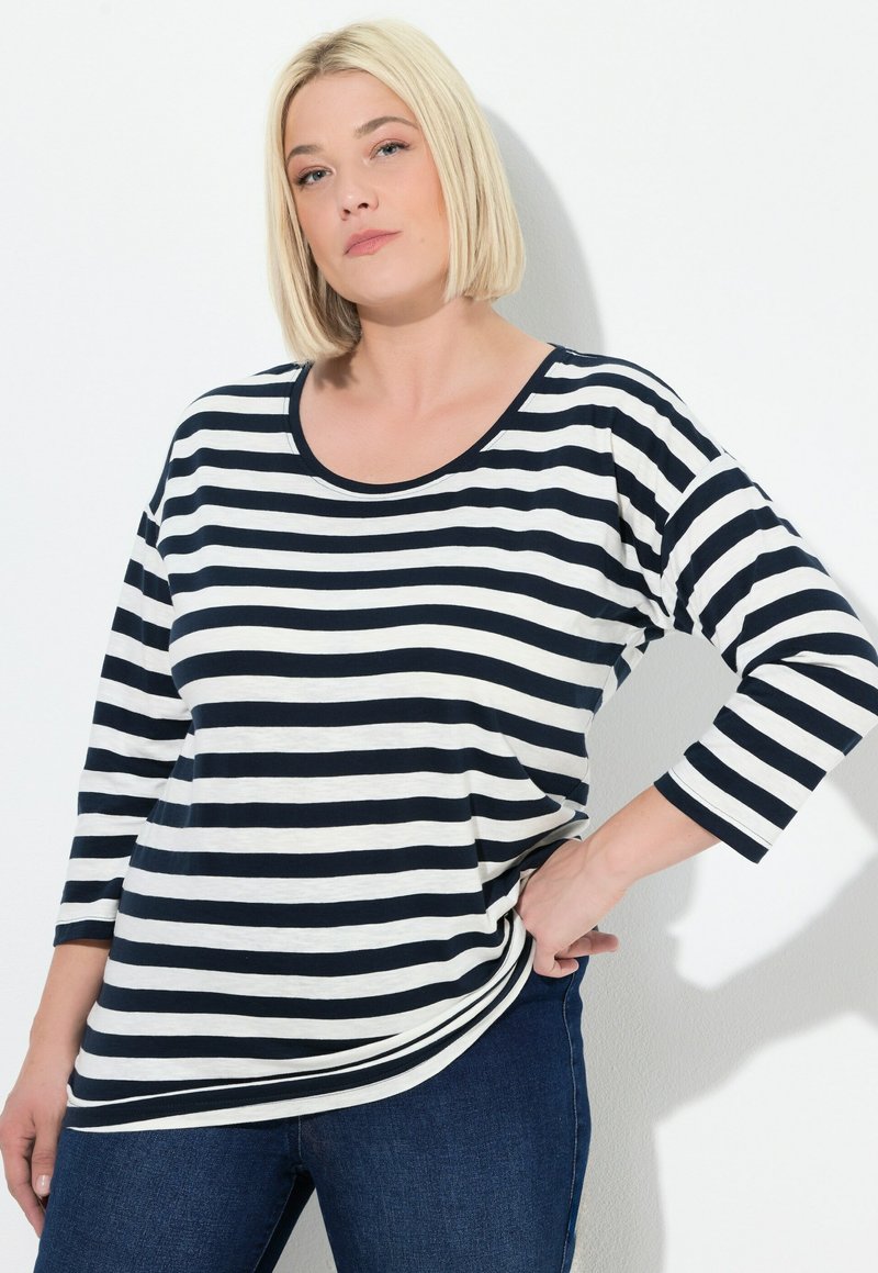 Marineblau und weiße gestreifte Langarmbluse mit rundem Ausschnitt und lockerer Passform, kombiniert mit dunkelblauen Jeans. Aus weichem Baumwollmaterial, ohne Verzierungen.