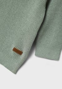 Maglione lavorato a maglia verde chiaro con un motivo testurizzato, polsini a costine e un'etichetta in pelle marrone sul lato sinistro in basso.