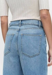 Vaaleansiniset farkut, joissa on korkea vyötärö, kaksi takataskua ja ommeltu yksityiskohtia. Yhdistetty ribbaavaan vaaleankerman väriseen toppiin.