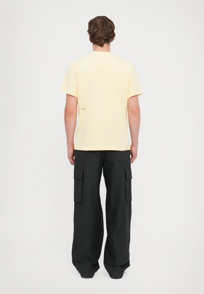 Tricou galben din bumbac, cu mânecă scurtă și guler rotund, asortat cu pantaloni cargo negri, lejere, care au mai multe buzunare și o textură distinctă.