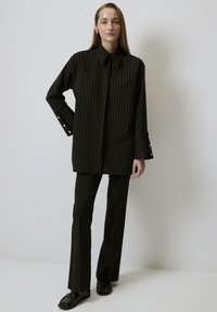 Zwart gestreept shirt met een puntige kraag en knopenmanchetten, gecombineerd met zwarte flared broek en loafers. Soepele stoftextuur.