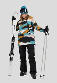 Sprzęt narciarski składający się z kurtki w wielokolorowy wzór, czarnych spodni, nart i kijków. Kurtka ma przednią kieszeń i ściągacz na dole.