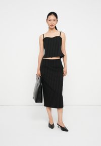 Conjunto negro de dos piezas que incluye un top corto con tirantes finos y una falda lápiz de longitud media, ambos con rayas verticales blancas.