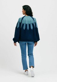 Stickad tröja med rundad hals, gradient i blå-grön färgskala och lös passform. Kombinerad med ljusblå jeans och vita sneakers.