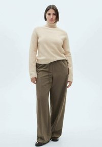 Lys beige turtleneck sweater lavet af blødt stof, parret med højtaljede brune bukser med vidde. Outfittet har en afslappet pasform og subtile teksturer.