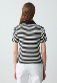 Polo a maniche corte a righe con texture a coste bianco e nero, con colletto nero a contrasto e design aderente.