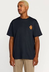 Sort bomuld t-shirt med korte ærmer, med et lille orange grafisk motiv på venstre bryst. Klassisk rund hals.