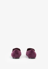 Ballerine in suede viola con punta arrotondata e discreti dettagli embossati sui lati. Suola in gomma nera visibile dalla vista posteriore.