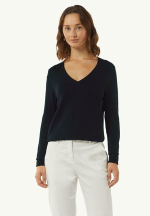 Black v-neck sweater with long sleeves, made from a smooth material. Features ribbed cuffs and a relaxed fit, paired with white trousers.
