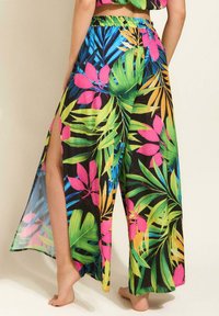 Luźne, lekkie spodnie z wyrazistym tropikalnym wzorem z dużymi zielonymi liśćmi i różowymi kwiatami na czarnym tle. Wysokie rozcięcia po bokach.