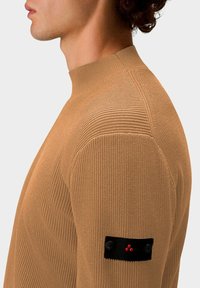 Brauner gerippter Strickpullover mit hohem Kragen, ausgestattet mit einem schwarzen Patch auf dem linken Ärmel, der rote Akzente und Knopfdetails aufweist.