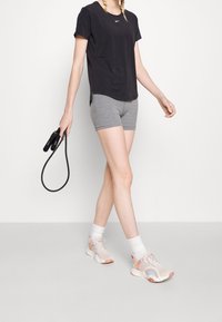 Ung person i svart Nike-t-shirt och grå shorts som går och håller ett svart hopprep i ena handen, iförd vita strumpor och sneakers.