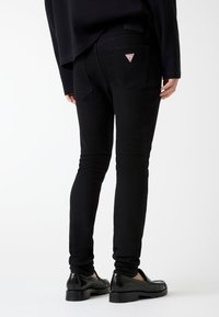 Czarne dżinsy z denimu o dopasowanym kroju, tylnych kieszeniach z trójkątnym logo i gładkiej fakturze. Noszone z czarnymi loafersami.