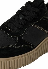 Svart sneaker med en blandning av mocka och strukturerat läder, runda svarta skosnören, stickade detaljer och en kraftig ribbad sula i beige.
