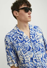 Camisa de manga corta en tonos de azul con patrón floral blanco. Hecha de tejido texturizado; presenta un cuello tipo camp y una botonera.