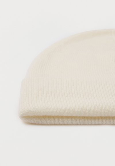 Krémszínű bordázott kötött, hajtott sapka puha anyagból, fehér felületen.