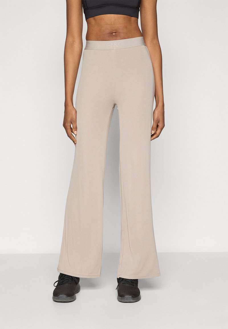 Bézs színű, bő szárú nadrág puha anyagból, széles derékpánttal és sima felülettel, fekete sportcipővel párosítva.