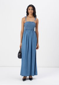 Jeans maxi-kjole med smocket bodice, justerbare stropper og en luftig silhuett. Båret med svart håndveske og spisse sko.