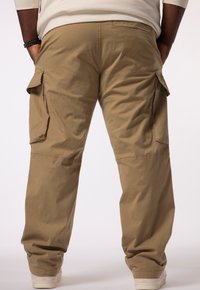 Khaki cargobroek van lichte stof, met grote zijzakken en een ontspannen pasvorm. Gestructureerd oppervlak met minimale details.