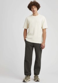 Chemise tricotée texturée à manches courtes crème associée à un pantalon fuselé vert foncé et des baskets beiges avec des accents réfléchissants.