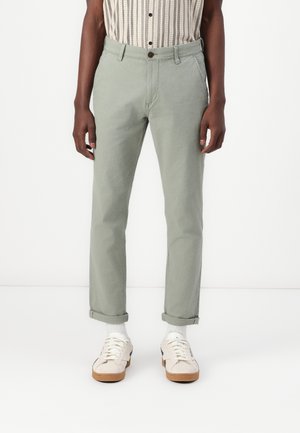 Light green cotton pants with a straight cut, featuring a button closure, front pockets, and rolled cuffs. Paired with white sneakers.