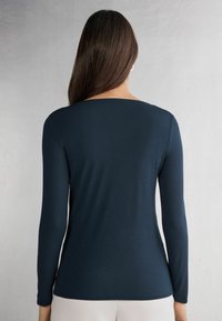 Marineblaue Langarmshirt mit Rundhals, glatter Textur und taillierter Silhouette, mit einem dezent abgerundeten Saum an der Taille.