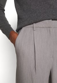 Grå uldblandede bukser med skræddersyet pasform, der har forreste læg, sidelommer og en glat tekstur. Parret med en mørkegrå sweater.