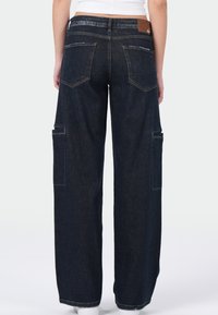 Donker denim cargobroek met een wijde pijpontwerp, voorzien van dubbele achterzakken en zijcargozakken, afgewerkt met een bruine leren label op de tailleband.