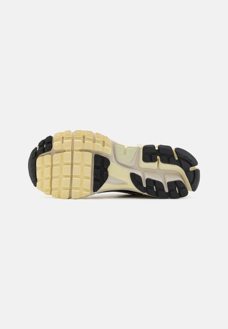 Semelle de chaussure de course avec un motif texturé. Présente un mélange de caoutchouc noir et jaune, avec un intermédiaire rembourré et un design de semelle d'adhérence qui offre un bon support.