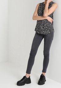 Černobílý top bez rukávů s puntíky a vzdušným dekoltem, doplněný tmavě šedými úzkými džíny a robustními černými teniskami.