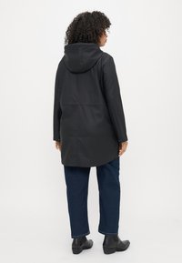 Svart huva regnjacka, slät textur, knälång design, med sidfickor och en avslappnad passform. Buren med raka mörkblå jeans.