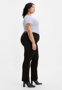 Ljusblå mönstrad kortärmad topp i kombination med svarta åtsittande jeans och svarta klackade ankelboots. Tatueringar synliga på armen.