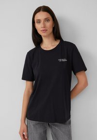 Czarna bawełniana koszulka z krótkim rękawem, okrągłym dekoltem i białym napisem na piersi brzmiącym "STAY SALTY, MY FRIENDS". Gładka tekstura.