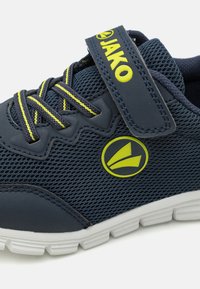 Chaussure de sport en maille bleu marine avec des accents jaunes, dotée d'une sangle Velcro, d'une surface texturée et d'une semelle en caoutchouc blanc avec un motif de semelle.